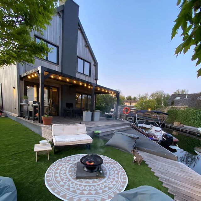 Moderne zwarte houten pergola met sfeerverlichting aan een woning bij het water. Stijlvolle overkapping zonwering. pergola koppelstukken rijpex